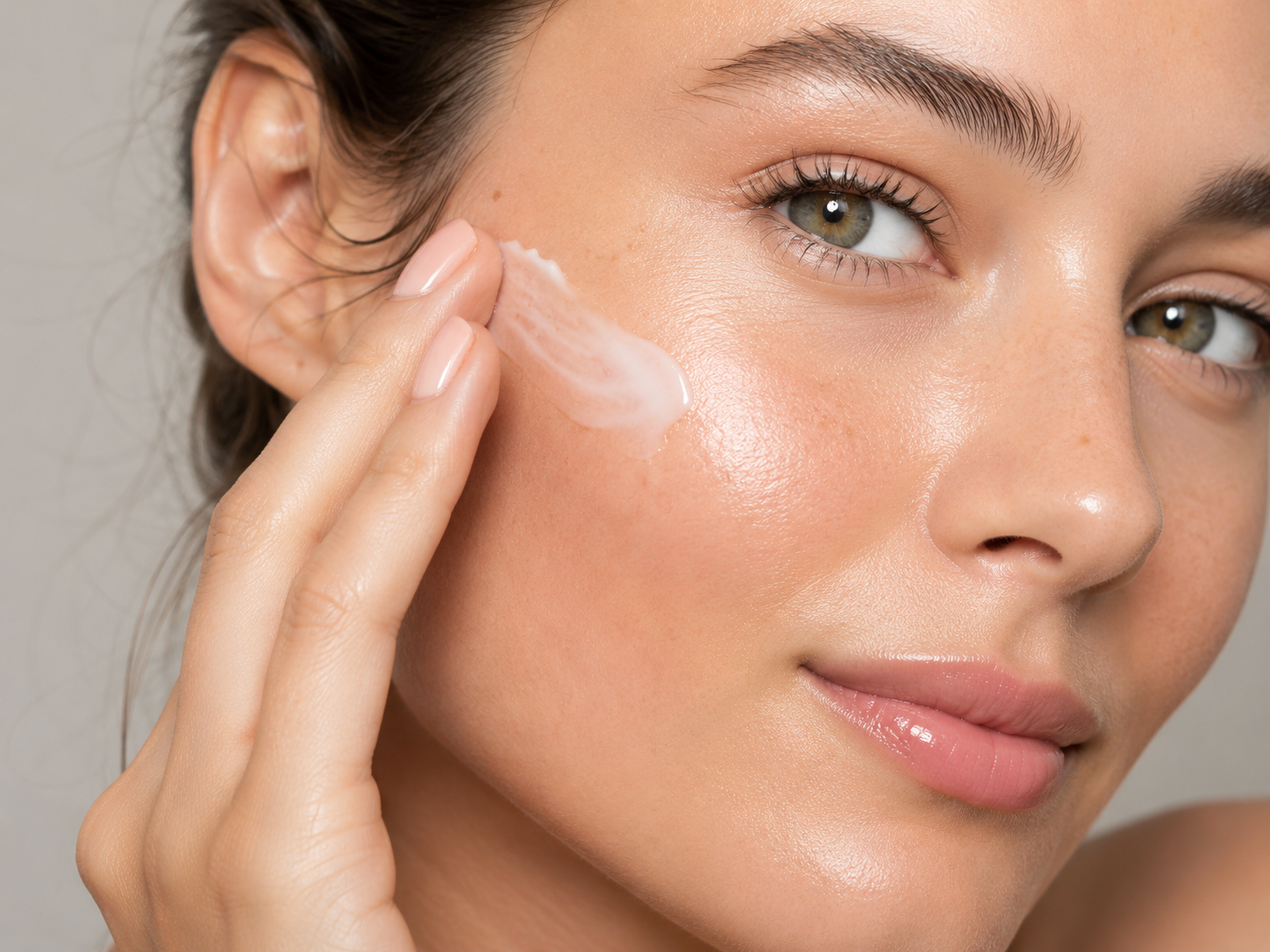 A woman smoothing a pale cream onto her cheek with her fingertips