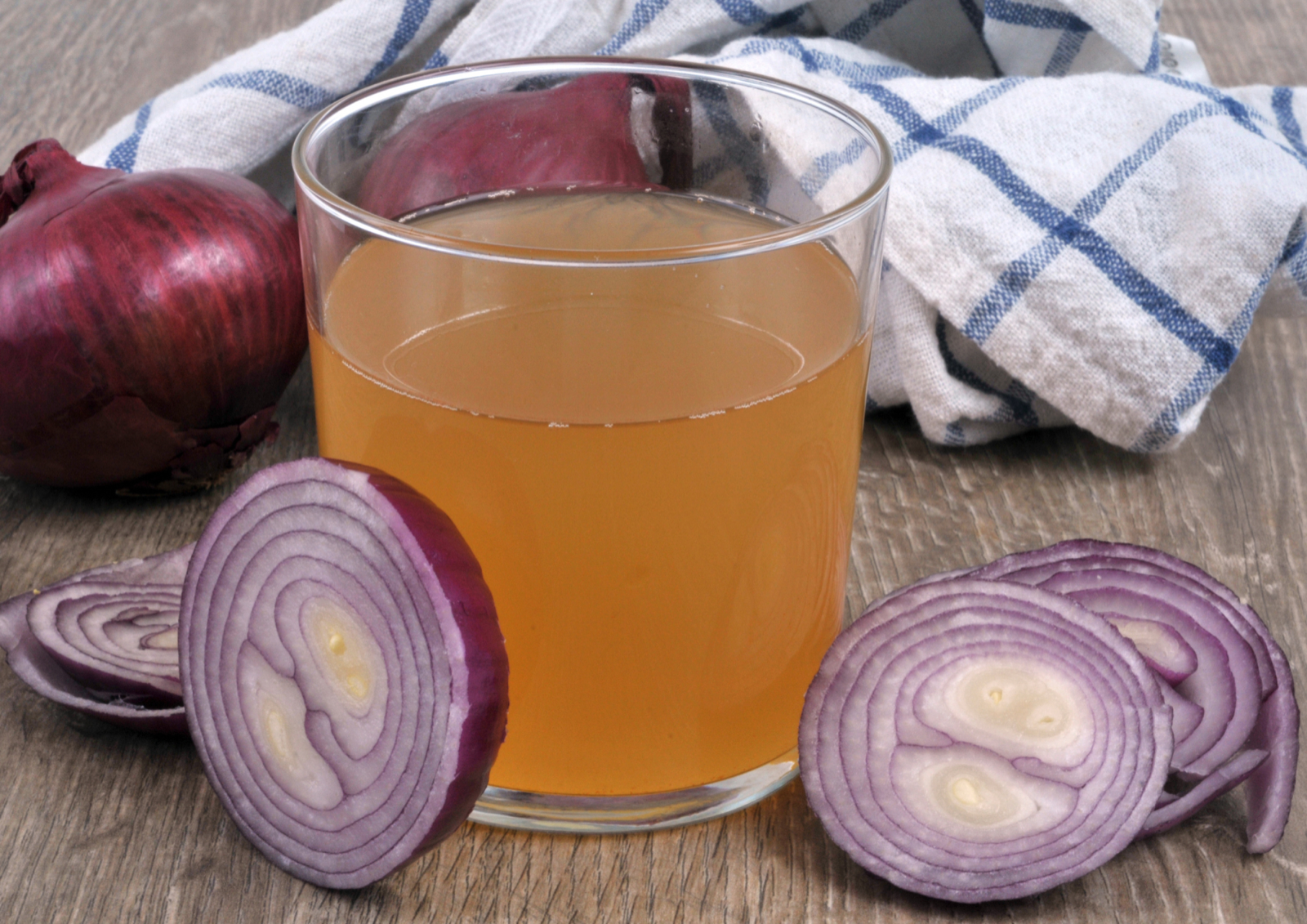 A glass of freshly pressed onion juice beside a halved red onion and onion slices on a wooden table