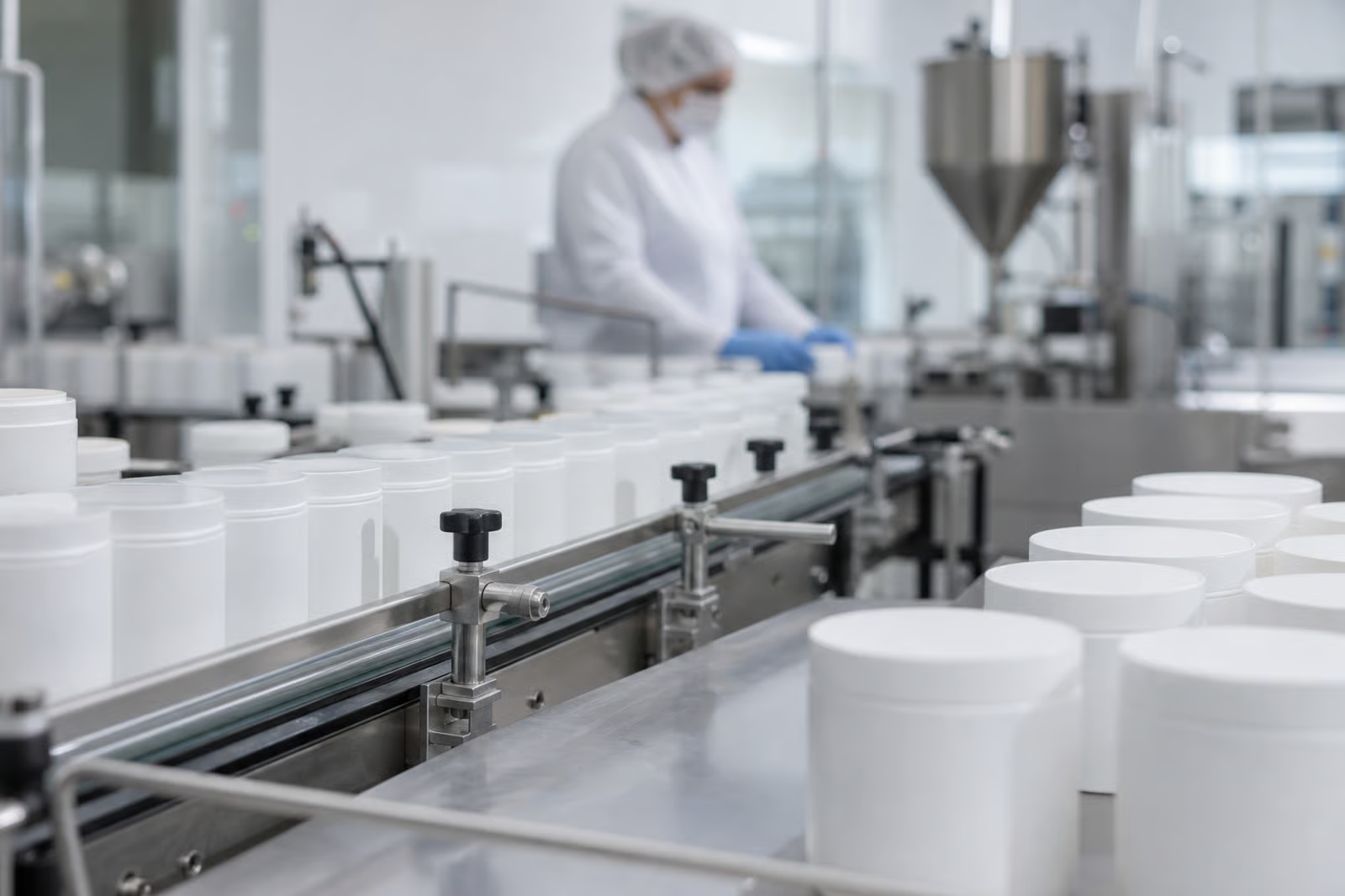 Identical white jars moving down a contract manufacturing line as a worker fills them