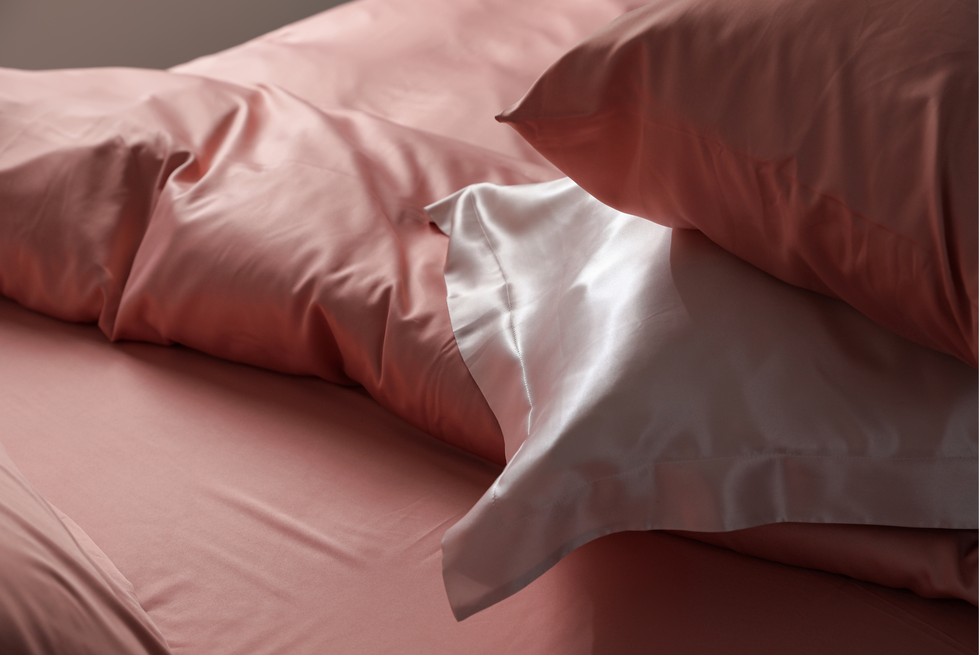 A white silk pillowcase draped over pink cotton bedding, the two fabrics side by side