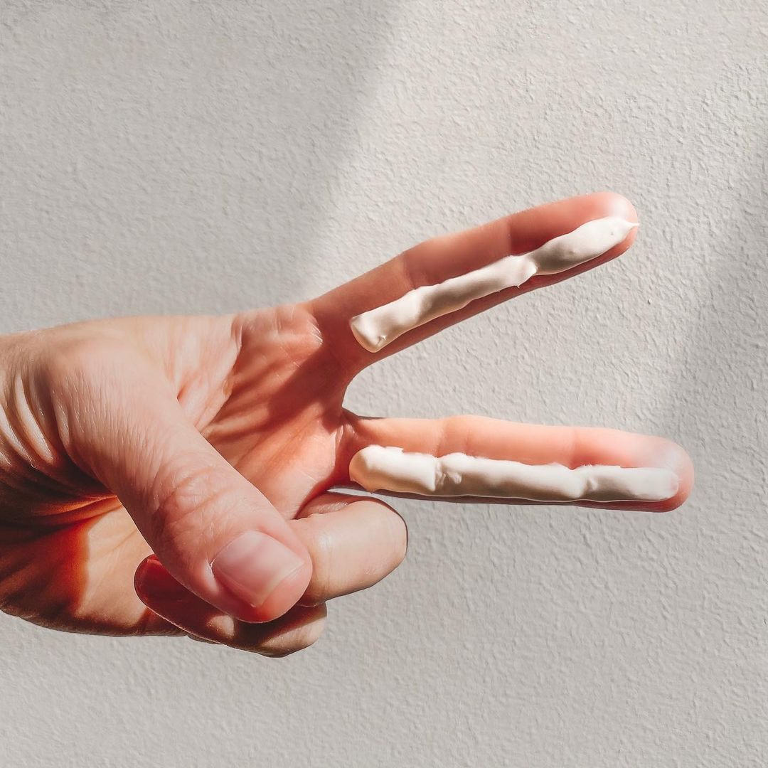 A hand held up in sunlight with a stripe of sunscreen along the index and middle fingers